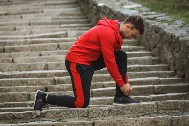 Man in sportswear tying his shoe on stone steps